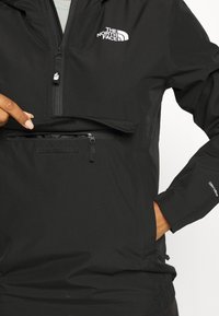 Czarna kurtka z suwakiem na ćwierć długości, wyposażona w zapinaną na suwak kieszeń i miękką klapę na rzep. Wykonana z lekkiego, trwałego materiału.