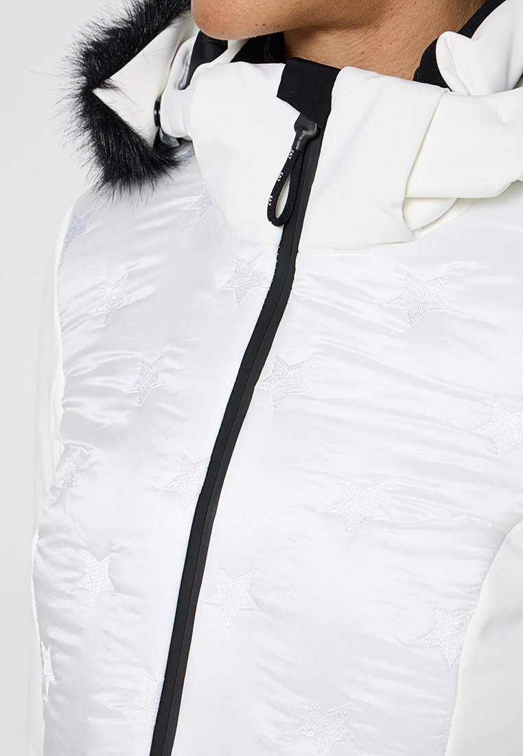 Giubbotto bianco trapuntato con motivi a stella, una cerniera nera e un cappuccio con bordo in pelliccia nera. Tessuto lucido e testurizzato con una finitura morbida.
