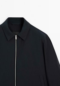 Black jacket with a collared neckline, featuring a silver zipper down the front. Made from a smooth material with minimal stitching details.