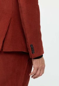 Rostfarbener, gerippter Cordblazer mit schwarzen Knöpfen am Ärmel. Nahaufnahme der Ärmeldetails, die die Textur und Farbe des Stoffs zeigt.