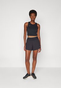 Svart atletisk crop top, matchande shorts med elastisk midjeband, och svarta löparskor. Har en logotyp på toppen och shorts.