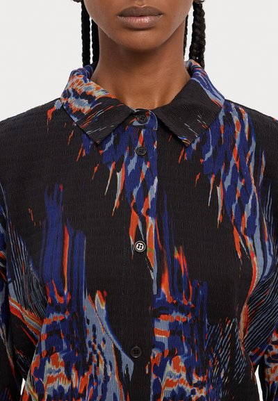 Fekete, gombos ing textúrált anyagból, mely merész absztrakt mintákkal bír kék, piros és fehér színekben, strukturált gallérral kiemelve.