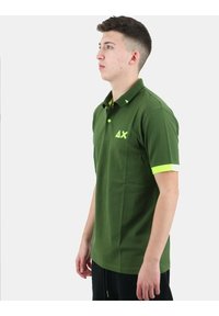 Polo verde in cotone, con colletto e accenti gialli sulle maniche. Presenta un logo giallo sul petto sinistro.