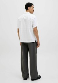 Camicia bianca a maniche corte con un motivo testurizzato, abbinata a pantaloni grigi larghi e scarpe scure, vista da dietro.
