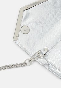 Coin d'une pochette argentée texturée avec un cadre métallique, un bouton-pression, et une bandoulière en chaîne argentée attachée par un crochet métallique.