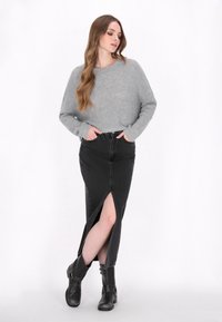 Szary sweter z dzianiny, czarna długa spódnica z denimu z bocznym rozcięciem, stylizowana z czarnymi botkami za kostkę. Prosty design, swobodna tekstura, dopasowany kształt.