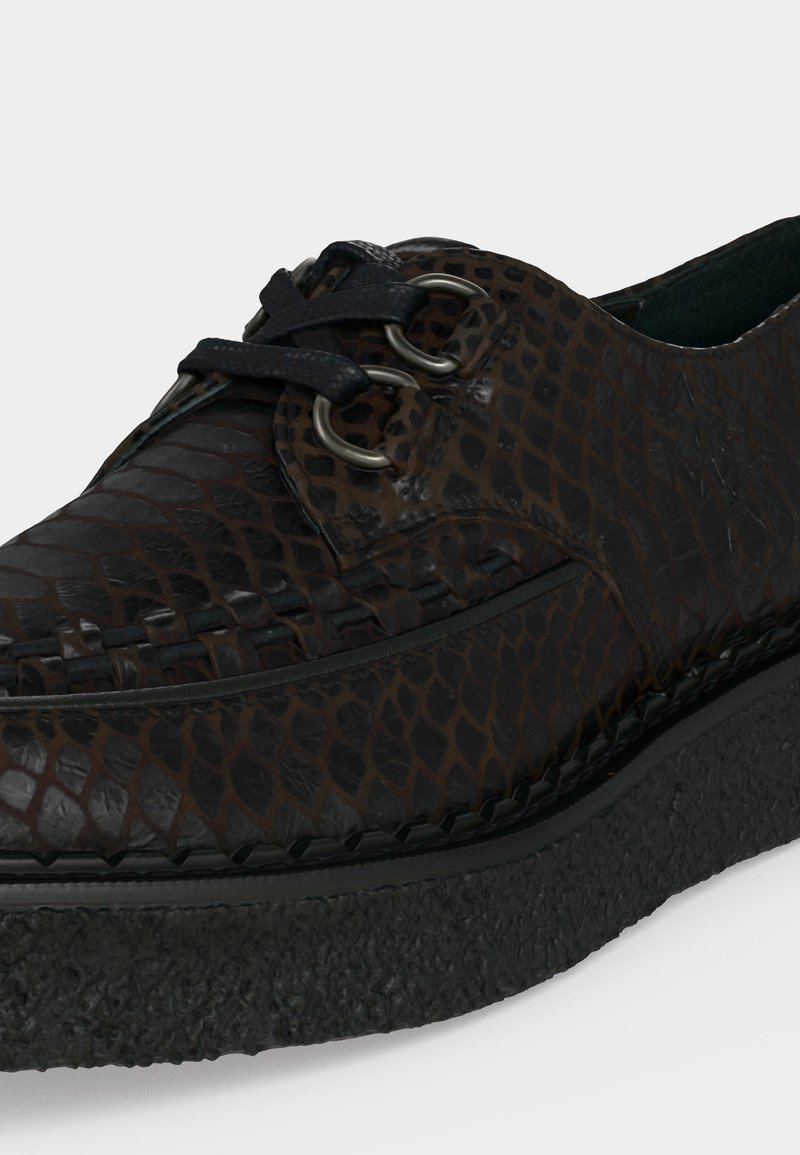 Dunkelbrauner Lederschuh mit strukturiertem Schlangenledermuster, schwarzen Schnürsenkeln, die durch silberne Ösen gezogen sind, und einer dicken schwarzen Gummisohle.