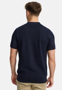 Polo shirt à manches courtes navy en tissu tricoté texturé avec col et ourlet côtelés, présentant une coupe épurée et un design sobre.