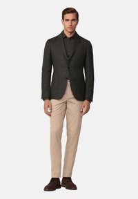 Blazer grigio scuro con vestibilità slim, due bottoni e rever a scollo, abbinato a pantaloni beige e scarpe marroni, su uno sfondo bianco.