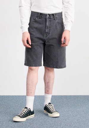 Pantalones cortos de mezclilla grises con una cintura alta y corte recto. Bolsillos frontales, cierre de botón y dobladillo limpio. Combinados con zapatillas oscuras y calcetines blancos.