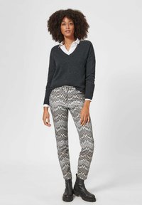 Dunkelgrauer V-Ausschnitt-Pullover, darunter ein weißes Hemd mit Kragen, kombiniert mit gemusterten grau-weißen Zickzack-Hosen und schwarzen Knöchelstiefeln.