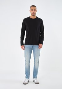 Black long-sleeve shirt paired with light blue jeans and white sneakers with black and gray accents. Simple, casual design with fitted silhouette.