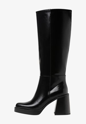 Schwarze knöchelhohe Stiefel aus glänzendem Material, mit einem klobigen Blockabsatz und einer runden Zehenpartie. Nahtdetails verlaufen entlang der Außenseite.