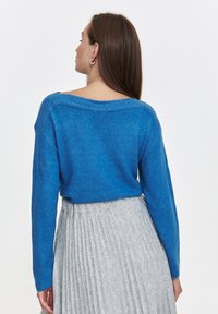 Niebieski sweter dzianinowy z luźnym dekoltem i długimi rękawami, w połączeniu z plisowaną szaro-skalną spódnicą. Miękka tekstura, lekko oversize'owy krój.