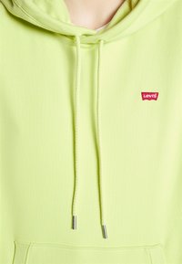 Limegrønn hettegenser med snor, med en liten rød Levi's-logo. Den har en myk tekstur og en frontlomme til å stikke hendene i.