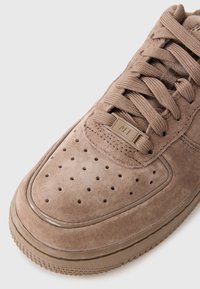 Baskets en daim marron avec un bout perforé, des lacets ton sur ton et une semelle en caoutchouc. Présente une petite étiquette en métal et des détails de couture contrastants.