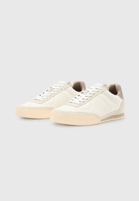Sneakers bianchi in pelle con un'accente testurizzata beige, caratterizzati da suola in gomma, punta rotonda e sei fori per i lacci.