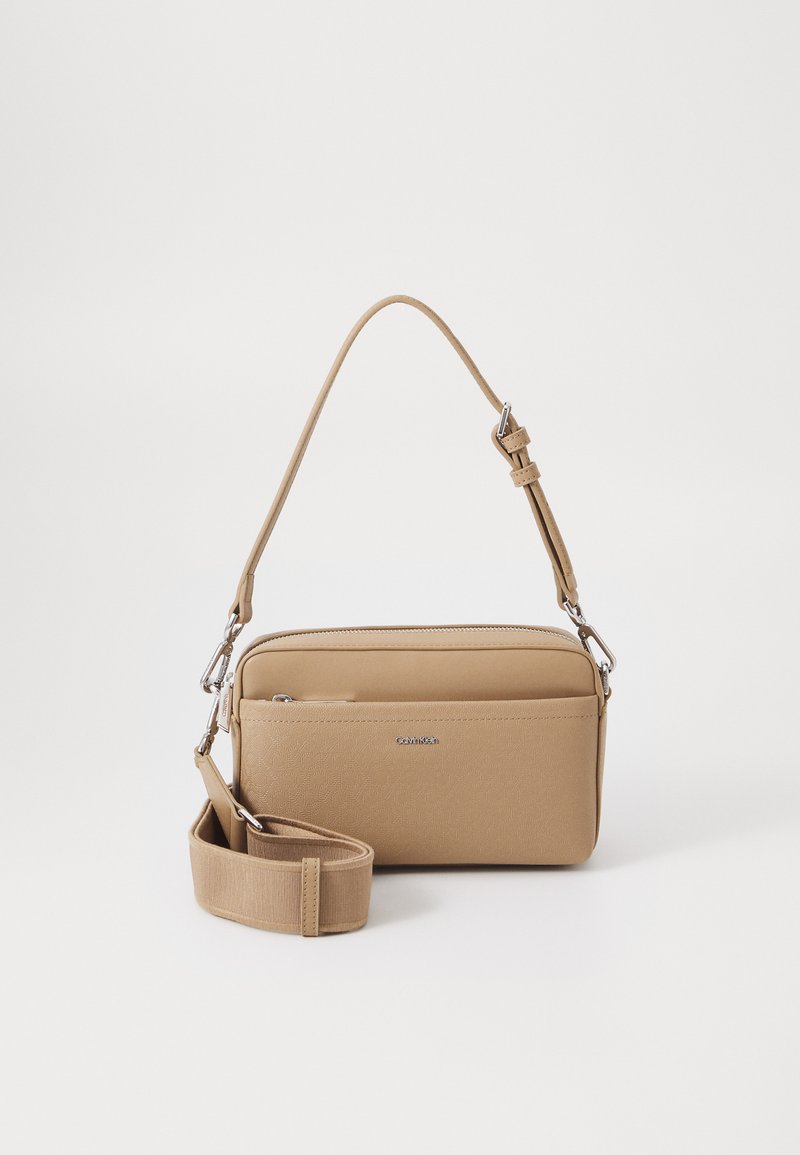 Tan crossbody bag made of synthetic material with a smooth texture. Features a detachable strap and silver hardware accents. Two zippered compartments.