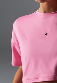 Rosa, gekürztes Sportoberteil aus glattem Material, mit kurzen Ärmeln und einem kleinen schwarzen Logo in der Mitte, sowie durchbrochenen Details am Saum.