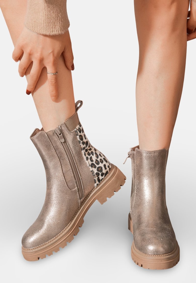 Bottines argentées métalliques avec une finition texturée, panneau latéral en imprimé léopard et semelle extérieure robuste à crampons. Fermeture zippée sur le côté pour un enfilage facile.