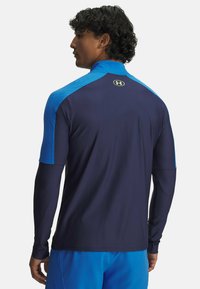 Navy long-sleeve athletic shirt with blue shoulder accents and a small logo on the upper back. Smooth texture, fitted design, and full coverage.