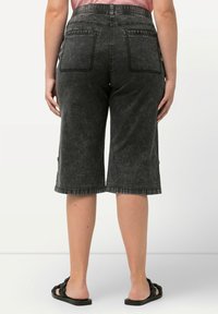 Mustat denimpitkät shortit, joissa on haalistunut pesu, korkea vyötärö ja kaksi takataskua. Hieman purkautuva yksityiskohta helman viimeistelyssä.