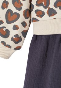 Langärmliges Oberteil mit cremefarbenem Grund und orange-grauem abstraktem Herzmuster, kombiniert mit einem Rock oder einer Hose aus dunklem strukturiertem Stoff.