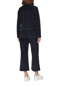 Granatowa kurtka z korduru i zestaw dopasowanych spodni. Strój charakteryzuje się luźnym krojem, skróconą długością i guzikami jako akcentami. Białe trampki dopełniają całość.