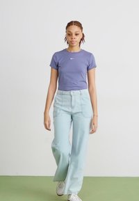 Violet trumpas rankovėmis marškinėliai su baltu Nike logotipu, derinami su šviesiai mėlynomis plačiomis kelnėmis. Apranga papildyta kasdiene balta avalyne.