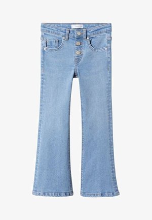 Niño con camiseta blanca de manga larga, vaqueros acampanados de talle alto en azul claro con botones, y zapatillas blancas, de pie contra un fondo liso.