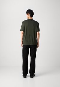 Mørkegrøn kortærmet t-shirt lavet af bomuld med rund halsudskæring. Kombineret med sorte, lige bukser og sorte sko.