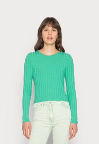 Camisola verde de manga longa com gola redonda. Tecido suave e design ajustado, combinado com calças de veludo cotelê verde claro.