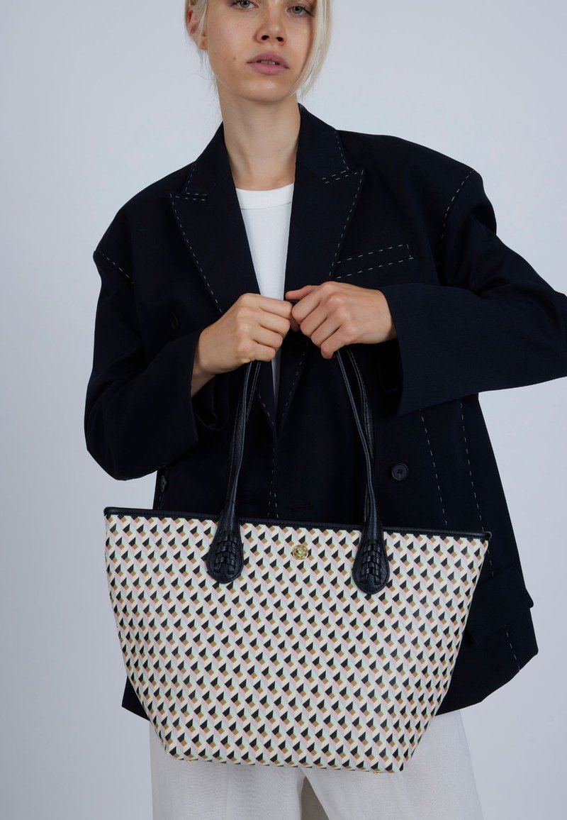 Mønstret mulepose med en cremefarvet bund, der har et geometrisk design i sort, grøn og koral, samt teksturerede sorte håndtag.