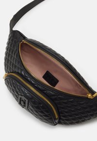 Musta tikattu nahkavyölaukku kultaisilla vetoketjuilla. Pääosasto on vuorattu vaaleanpunaisella kankaalla, jossa on pieni tuotemerkki.