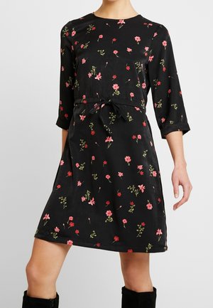 Sort knælængde kjole med pink og rød blomsterprint, trekvartærmer og bindebælte i taljen, båret med sorte støvler.