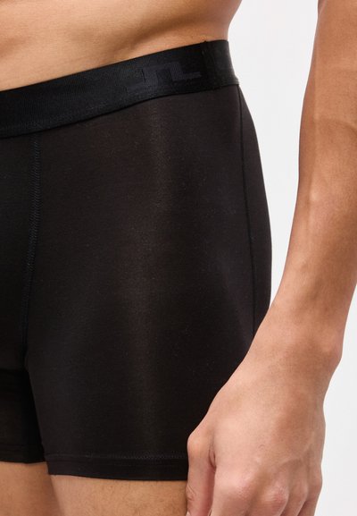 Κοντινό πλάνο ενός ατόμου που φοράει μαύρα εφαρμοστά μποξεράκια με διακριτικό μοτίβο στη μέση και ορατές ραφές στο πλάι.