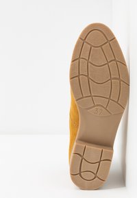 Scarpa gialla in pelle scamosciata con suola in gomma strutturata che mostra un motivo antiscivolo, taglia indicata come 37, con bordi lisci e punta arrotondata.