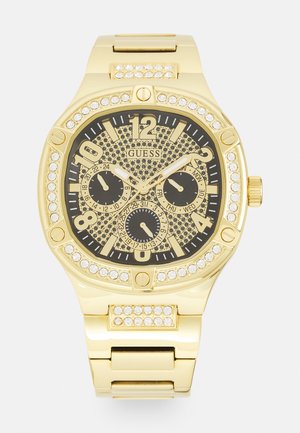 Montre dorée avec un cadran noir à motifs, ornée de cristaux, trois sous-cadrans et des index horaires bolds ; bracelet en maillons métalliques.