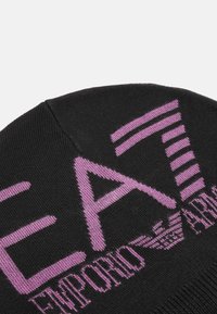 Juodas mezgimo kepurė, turinti violetinį logotipą su užrašu „EA7 Emporio Armani“. Dizainas apima vertikalias juosteles ir tekstūruotą apdailą.