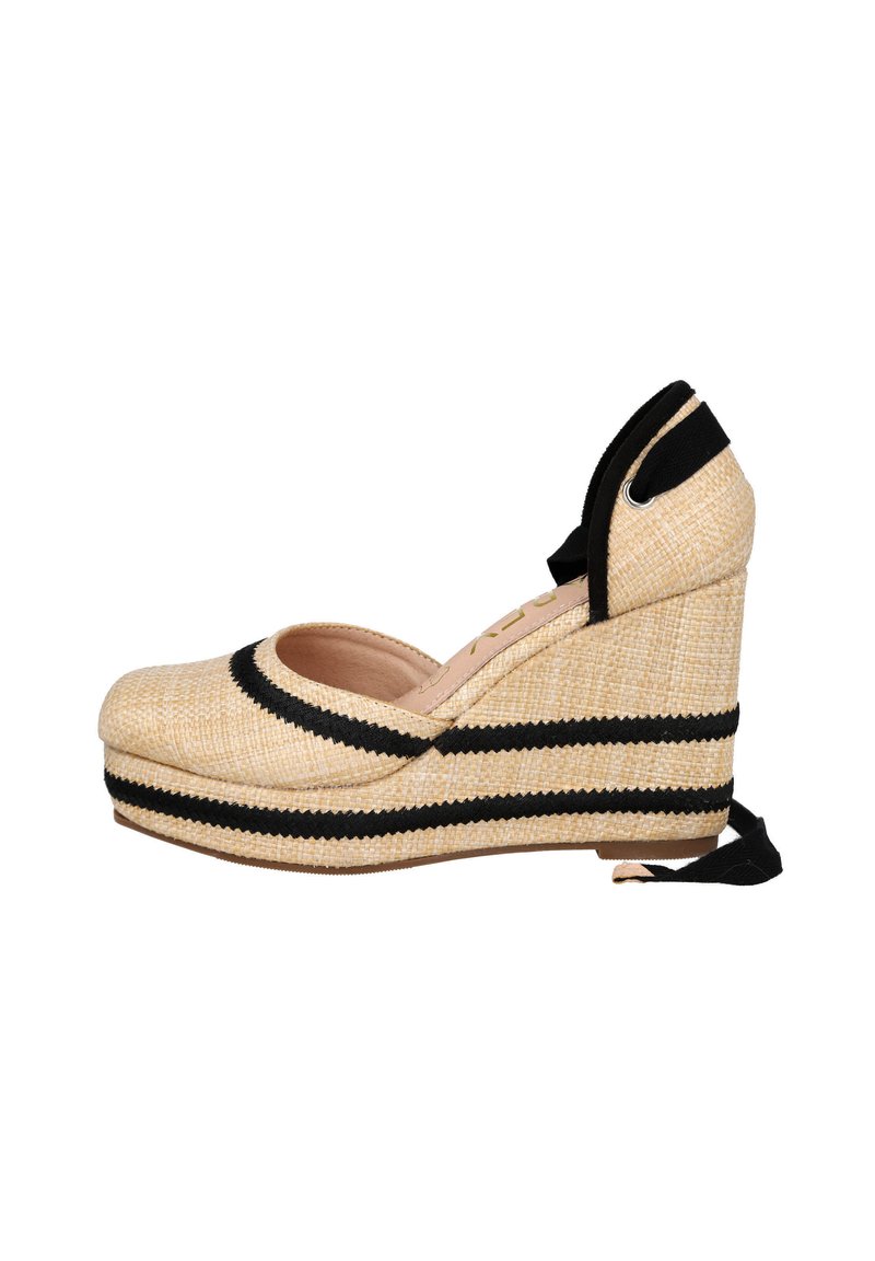 El zapato de cuña de esparto presenta un exterior similar al mimbre en beige con rayas negras, punta abierta y lazos de tela negra en el tobillo.