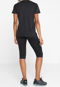 Camiseta deportiva negra de manga corta, combinada con leggins capri negros y zapatillas deportivas. Tejido suave y elástico, diseño minimalista.