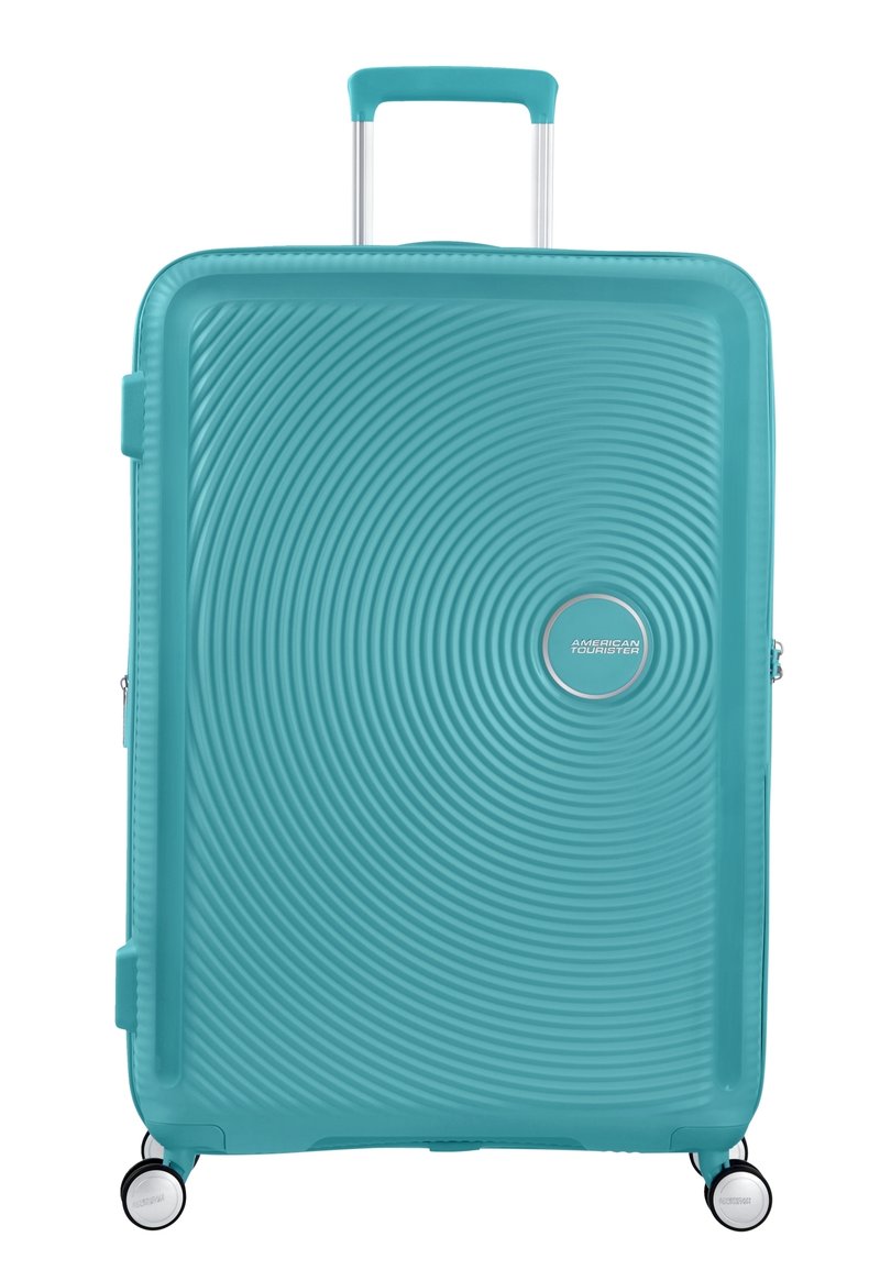 Valise rigide turquoise avec une texture striée, deux roues, une poignée rétractable et un logo circulaire à l'avant.