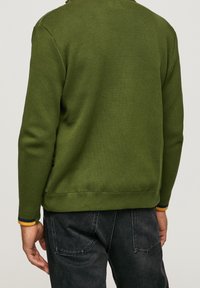 Grön stickad tröja med ribbat krage och ärmslut, med gula och marinblå ränder vid handleden och en bekväm passform.