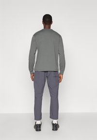 Γκρι πουκάμισο με μακριά μανίκια και στρογγυλή λαιμόκοψη, συνδυασμένο με γκρι παντελόνι που έχει πλευρική τσέπη, φορεμένο με μαύρα αθλητικά παπούτσια και λευκές κάλτσες.