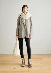 Blazer à carreaux beige et noir, assorti à une écharpe crème, un jean skinny noir et des bottes à lacets marron avec un intérieur en peluche ; sac fourre-tout léger.