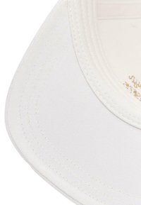 Gorra blanca con visera curva, detalles de costura y un forro interior con acentos dorados. La tela tiene un acabado suave y texturizado.