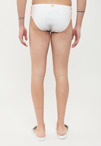Slip de bain blanc avec des accents orange, design ajusté, texture lisse et un petit logo sur la ceinture arrière. La vue de dessus révèle les jambes.