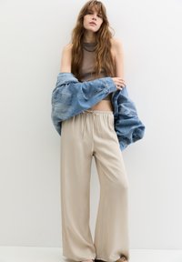 Beiga vida byxor med elastisk midjeband, tillsammans med en kort brun topp och en överdimensionerad blå denimjacka. Slät tygstruktur.
