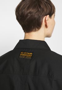 Giacca di denim nera con un patch del marchio vicino al colletto, con una finitura leggermente strutturata e design del colletto classico.