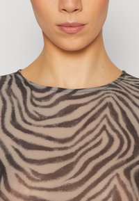 Transparente, figurbetonte Bluse in Beige mit schwarzem Zebra-Streifenmuster, Rundhalsauschnitt und strukturierter Stoffoberfläche mit einem weichen und glatten Finish.